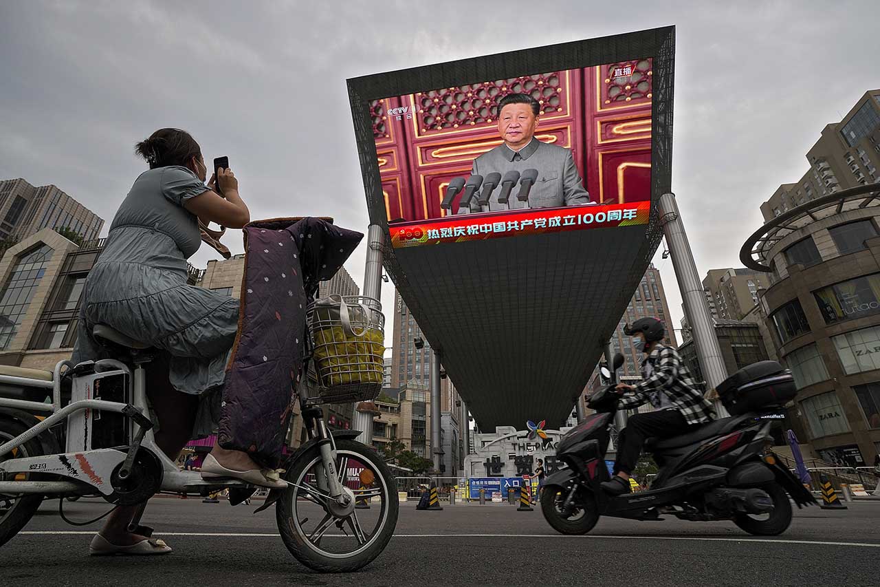 지난 7월 1일 중국 베이징의 톈안먼 광장에서 중국공산당 창당 100주년 기념행사가 열려 스쿠터를 탄 한 행인이 대형 비디오 스크린을 통해 연설하는 시진핑 주석의 모습을 찍고 있다. 베이징=AP