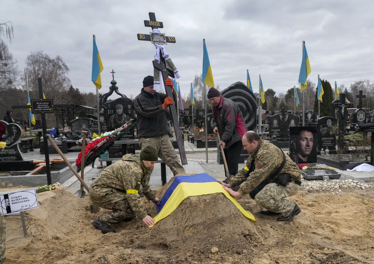 우크라이나 군인들이 5일(현지시간) 우크라이나 키이우의 한 공동묘지에서 러시아군에 의해 숨진 동료의 무덤에 국기를 덮어주고 있다. 키이우=AP