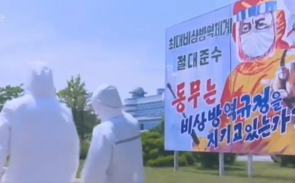 북한 방역요원들 뒤로 선전포스터가 보인다. 사진=시사주간 DB