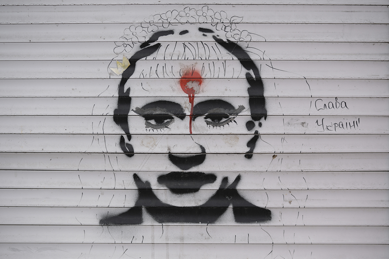 27일(현지시간) 우크라이나 스토얀카에서 러시아와의 전투로 피해를 본 한 상점 철문에 블라디미르 푸틴 러시아 대통령을 묘사한 낙서와 '우크라이나에 영광'이라는 문구가 쓰여 있다. 스토얀카=AP